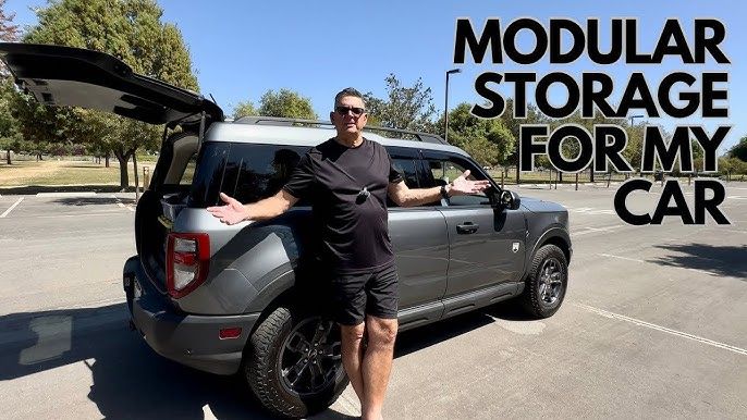 Man står bredvid en grå SUV med öppen baklucka och modulära hyllor